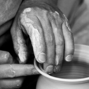 Artistic black and white close-up of hands shaping clay pottery on a wheel.
