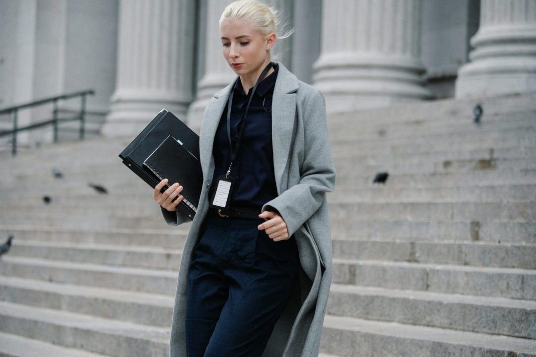Professional woman in formal attire walking down courthouse steps holding folders outdoors.