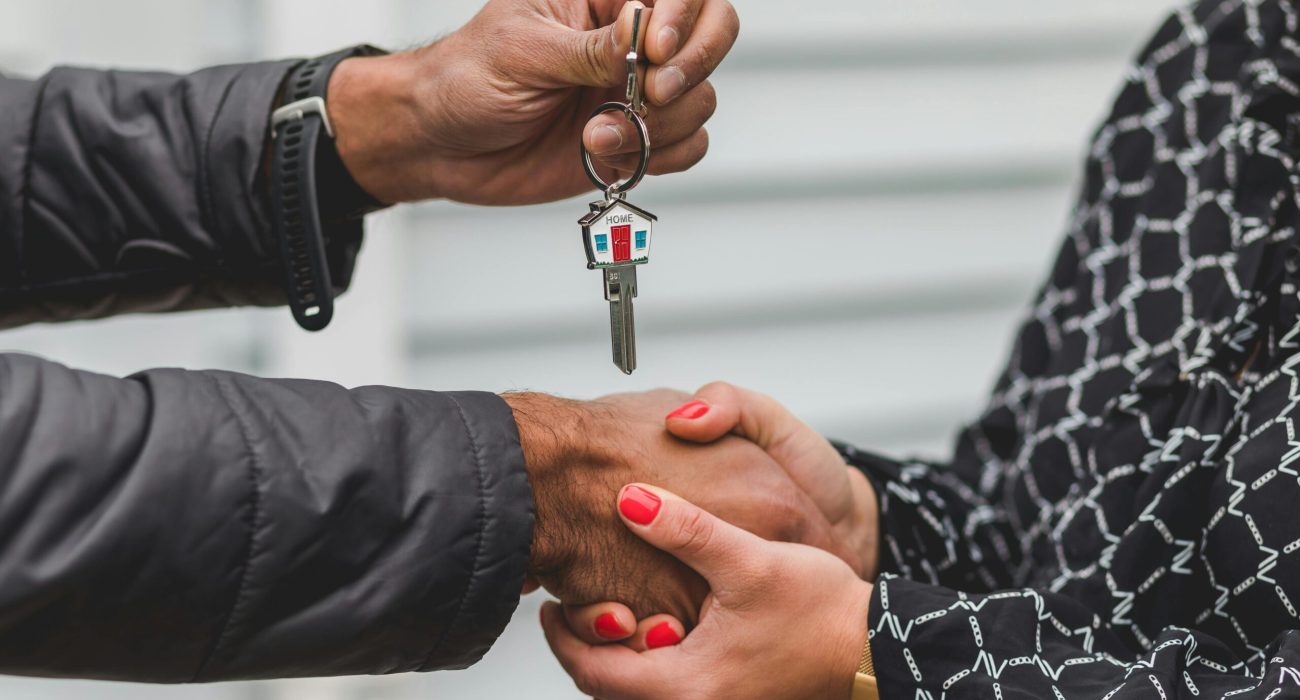 Close-up of a realtor handing over a house key to a new homeowner, symbolizing ownership and investment.